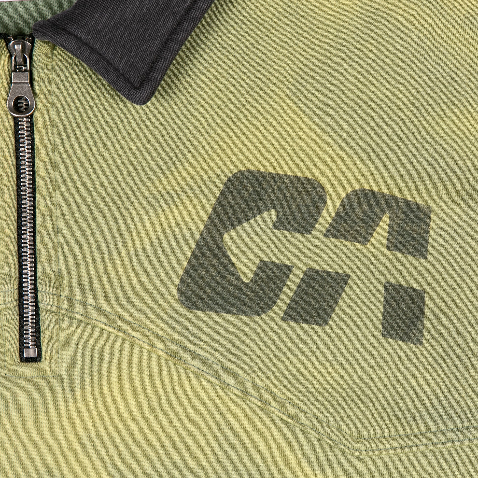 Bold "DA" graphic in faded black ink with arrow design, next to a metal zipper and black collar on the sweatshirt.