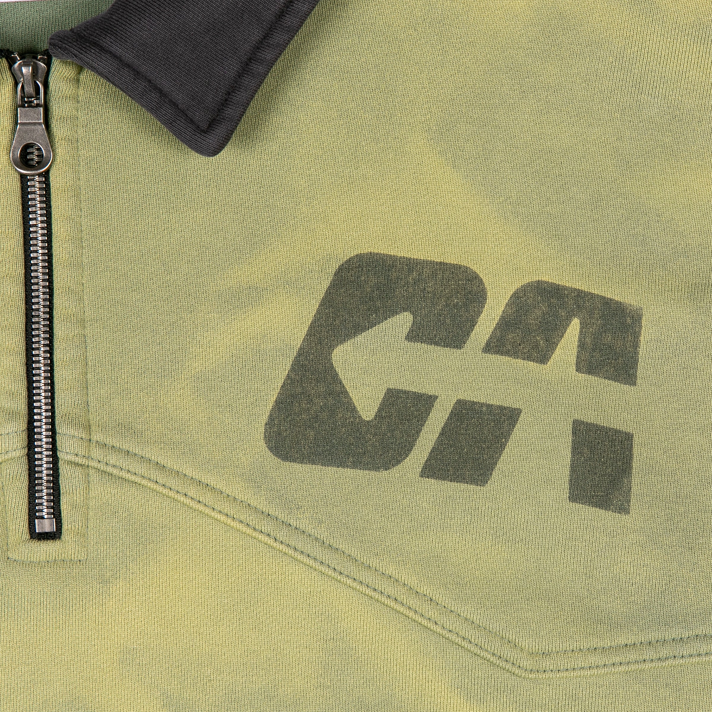 Bold "DA" graphic in faded black ink with arrow design, next to a metal zipper and black collar on the sweatshirt.